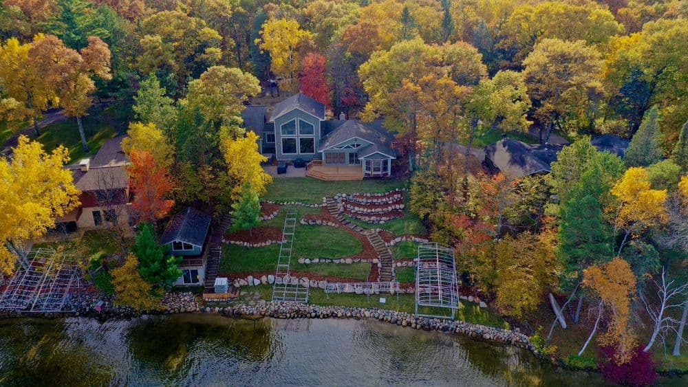 Aerial view of a lakeside home surrounded by vibrant fall foliage and landscaped garden.