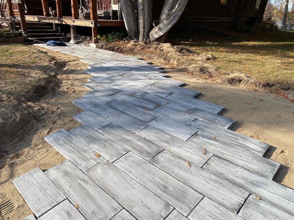 Wooden pathway leading to a deck, featuring staggered gray planks and surrounding sandy area.