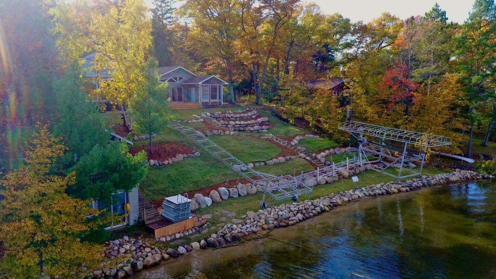 Aerial view of a lakeside home with colorful fall foliage and landscaped yard featuring rocks.