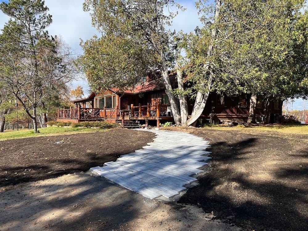 Rustic wooden cabin with a stone path surrounded by trees and landscaped grounds.