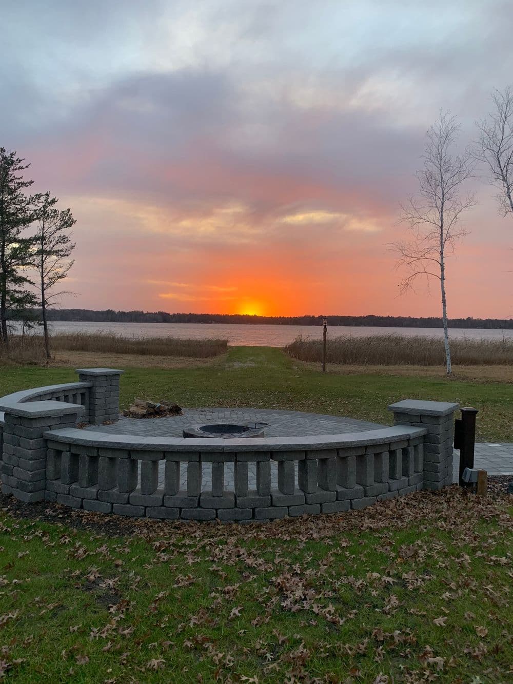 Scenic lakeside view with a stone firepit at sunset and colorful sky over tranquil water.