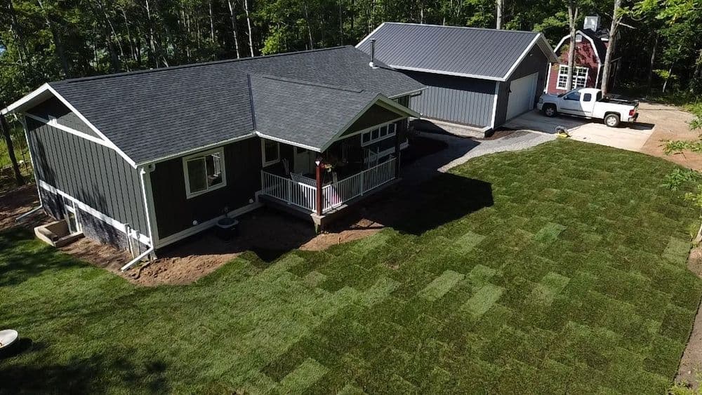 Modern house with fresh sod lawn and driveway, surrounded by lush trees and greenery.