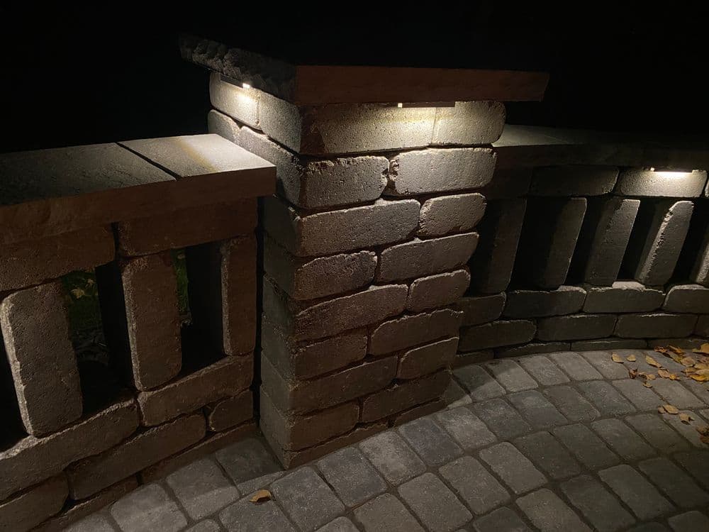 Illuminated stone railing at night with paver patio and warm lighting accents.
