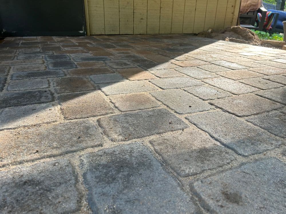 Newly installed paver stones create a durable outdoor patio surface. Sunlight casts shadows.