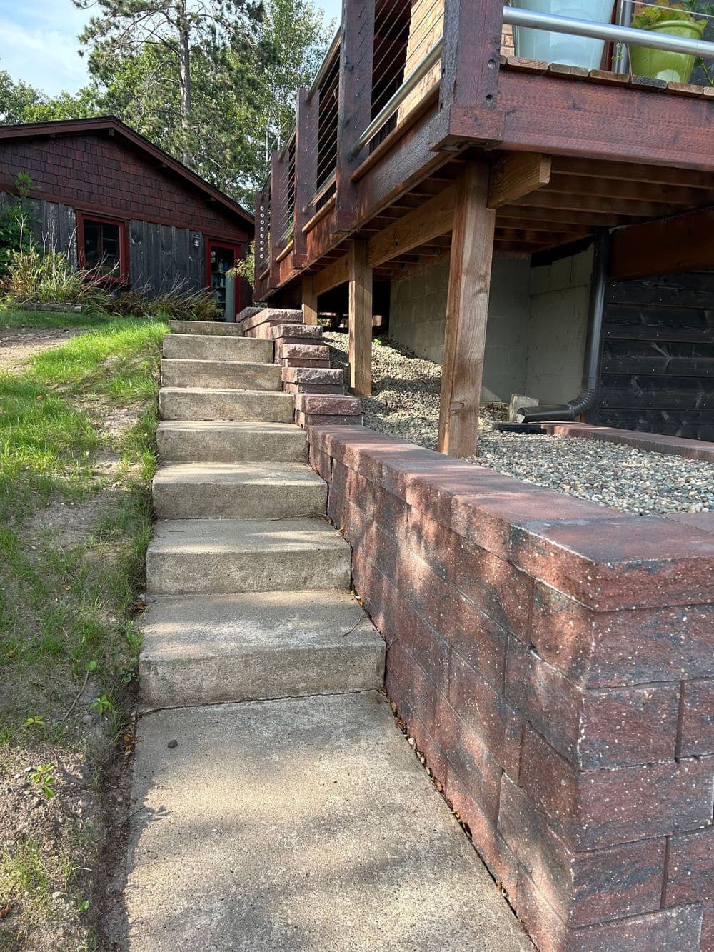 Concrete steps leading up to a wooden deck, surrounded by landscaping and a rustic cabin.