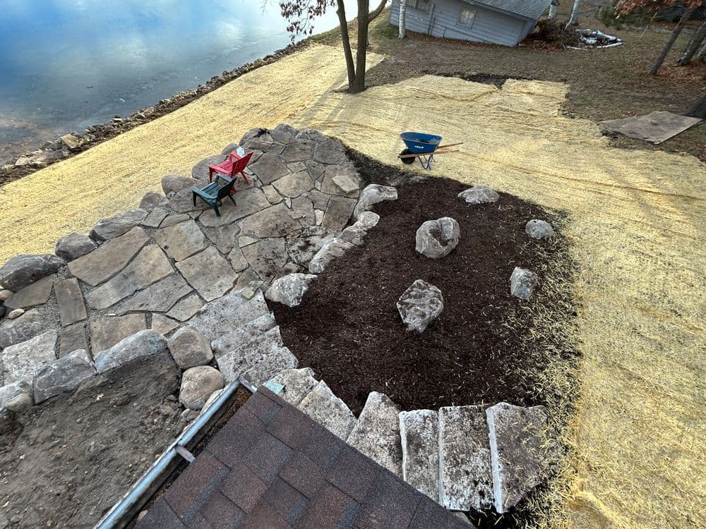 Landscape project featuring stone patio, mulch beds, and a wheelbarrow near a lake.