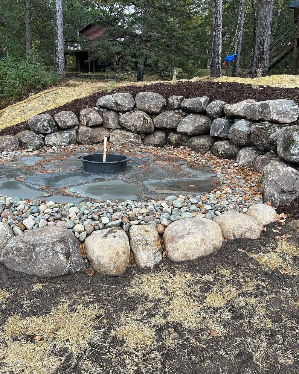 Rock centerpiece with smooth stones and a circular basin in a landscaped garden area.