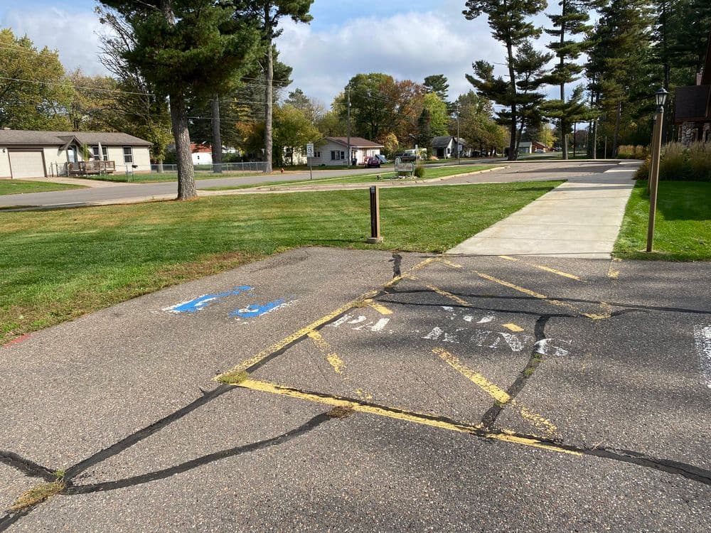 Cracked pavement with handicapped parking and no parking signs in a suburban area.