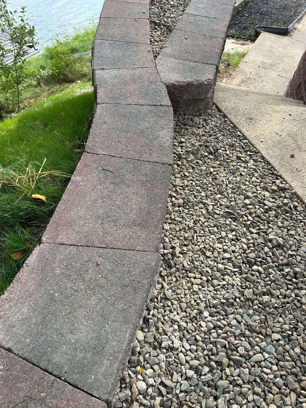 Curved stone pathway with gravel and grass beside a water feature.