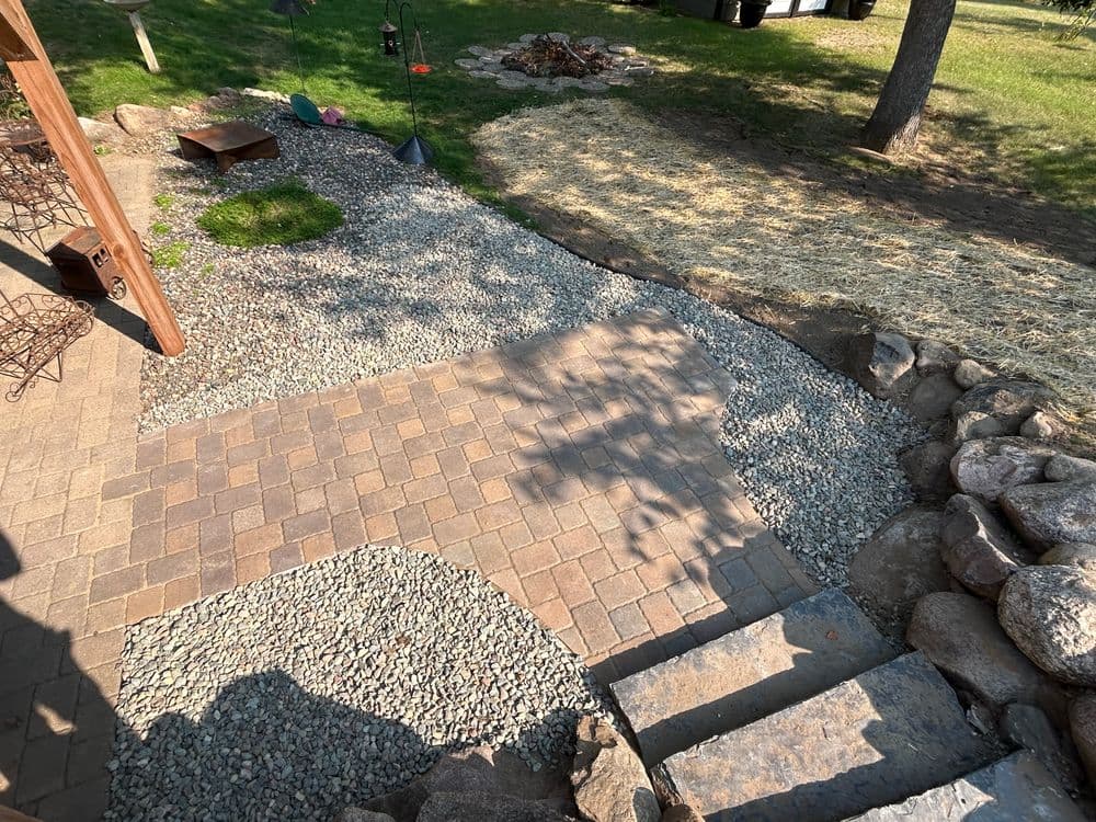 Landscape design featuring a stone patio, gravel pathways, and a fire pit area.