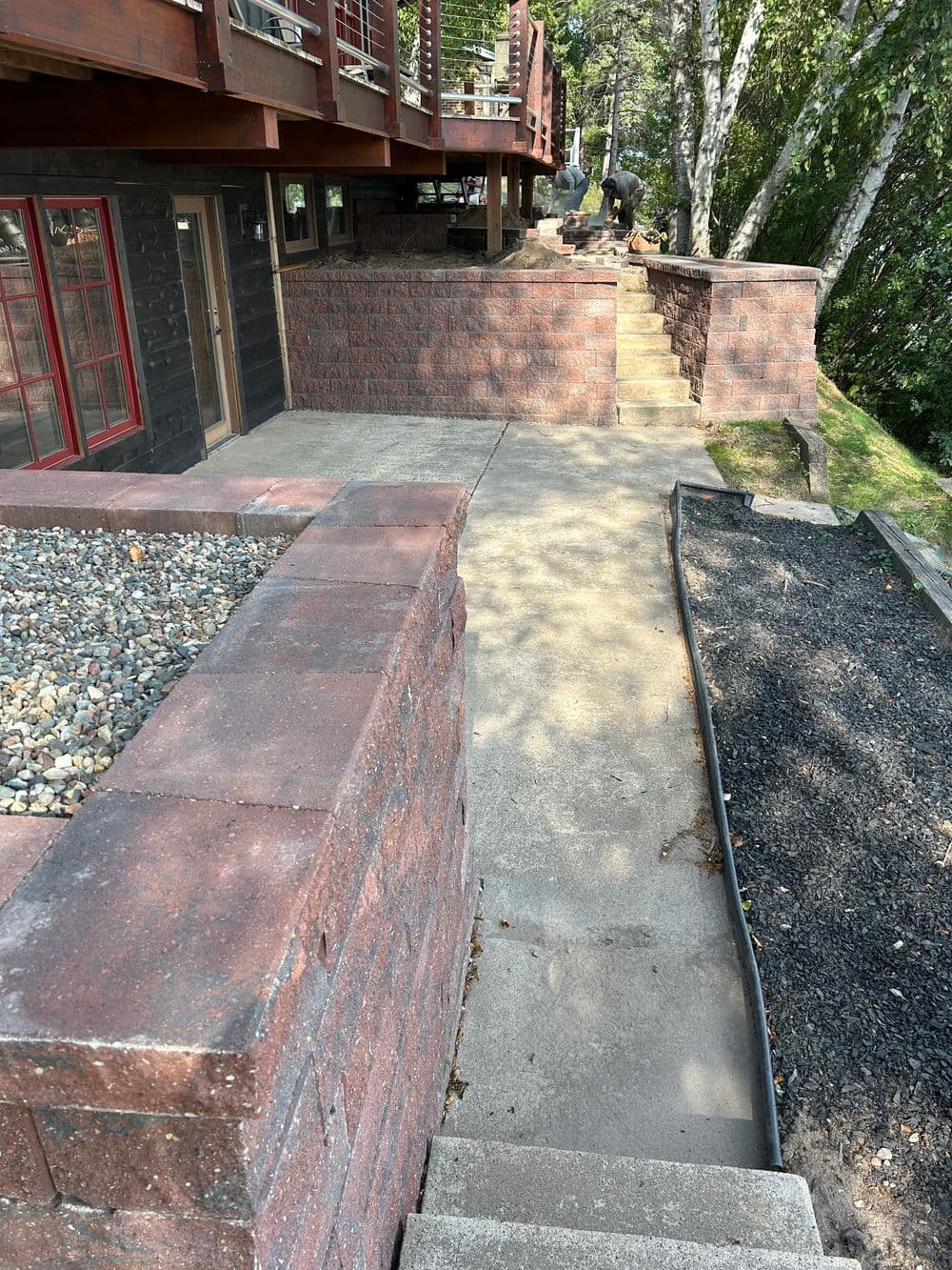 Pathway leading up to a wooden deck with stone walls and steps in a natural setting.