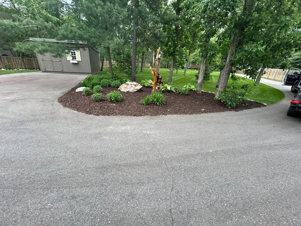 Landscaped circular driveway with mulch, rocks, trees, and greenery in a residential setting.