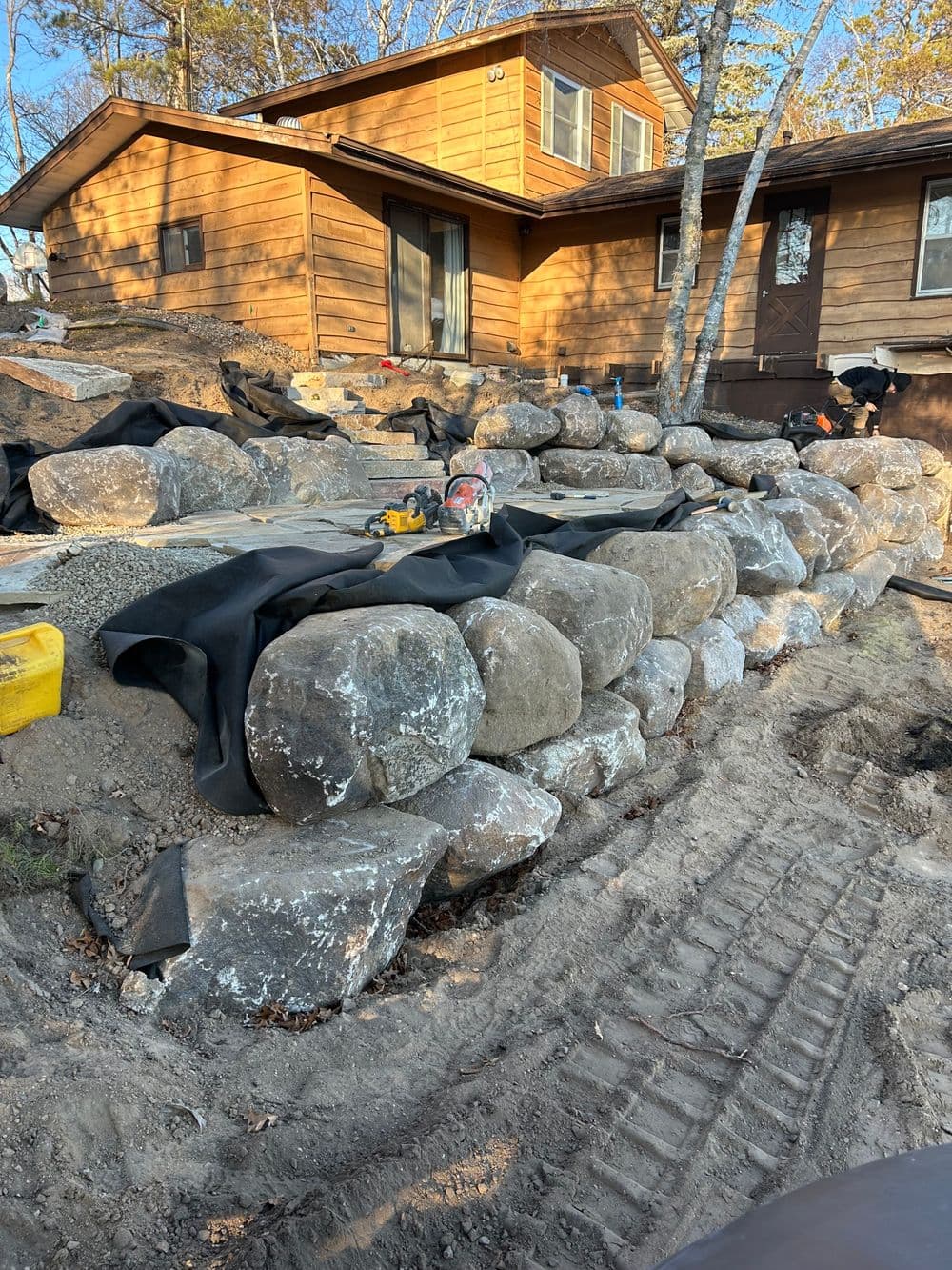 Outdoor landscape featuring large rocks along a home foundation, with landscaping fabric installed.