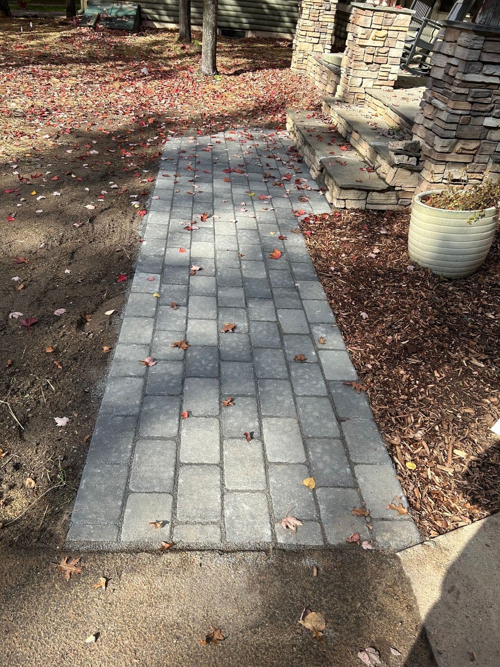 Paved walkway with leaves, leading to a stone steps and landscaped area.