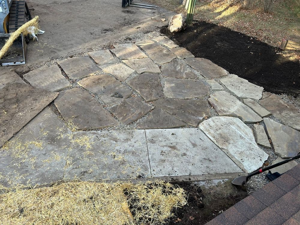 Natural stone patio installation with excavated ground and tools on site.