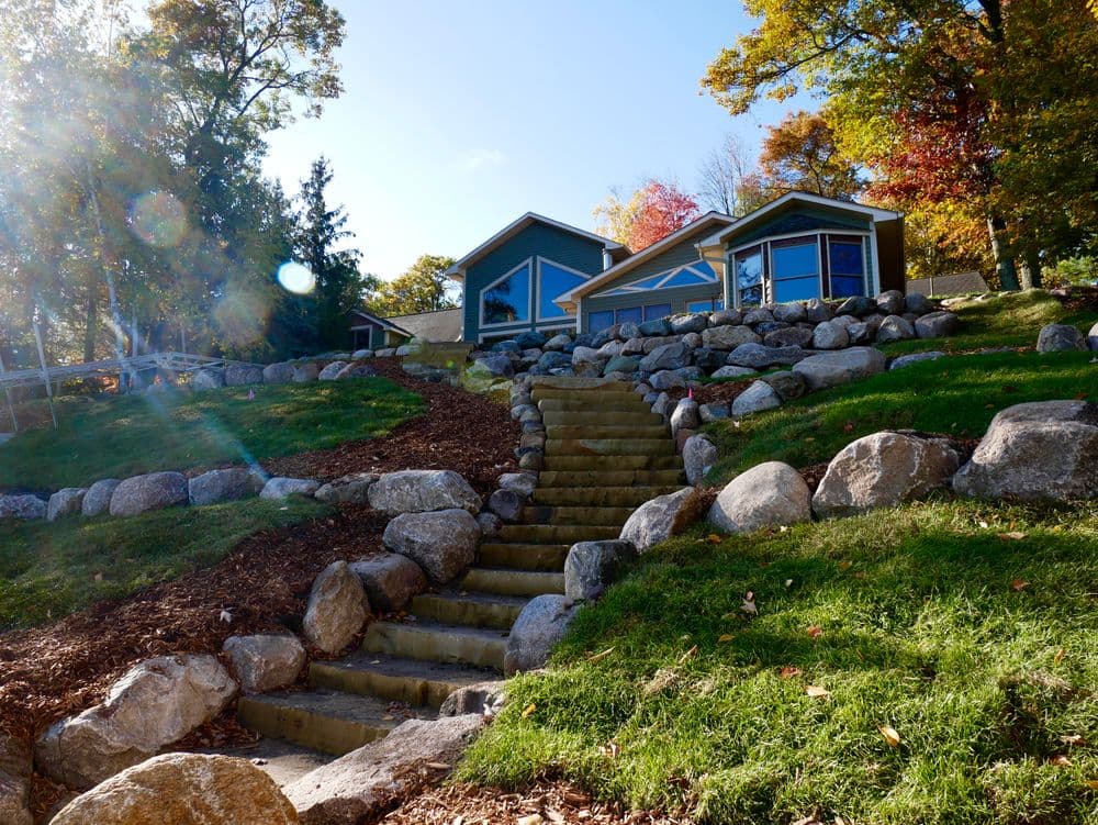 Modern house with stone steps, nestled in a vibrant autumn landscape. Green lawn and rocky terrain.