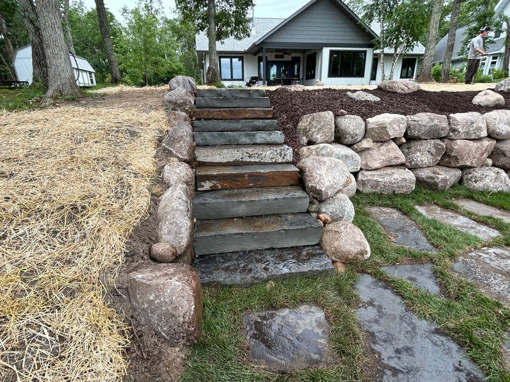 Stone staircase leading to a modern house with landscaped yard and boulder border.