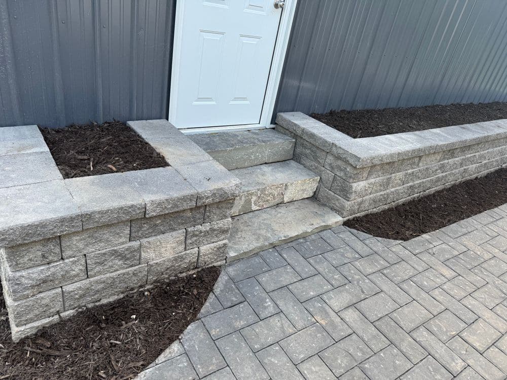 Stone steps and retaining wall with mulch at a building entrance, showcasing paver walkway.