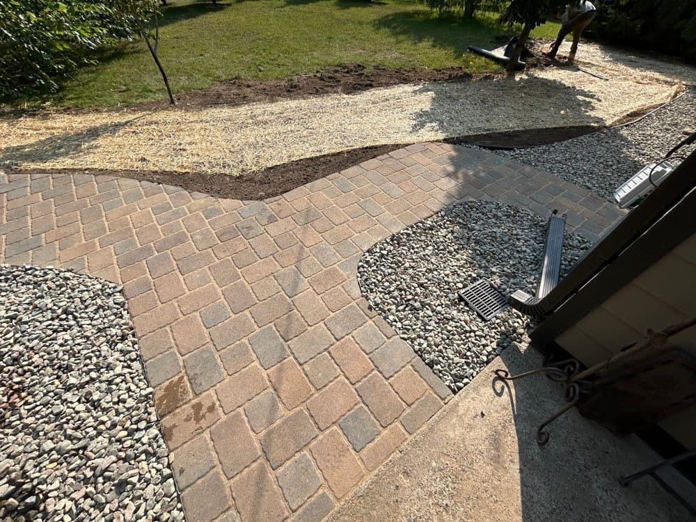 Curved paver pathway leading to a landscaped yard with fresh soil and gravel accents.