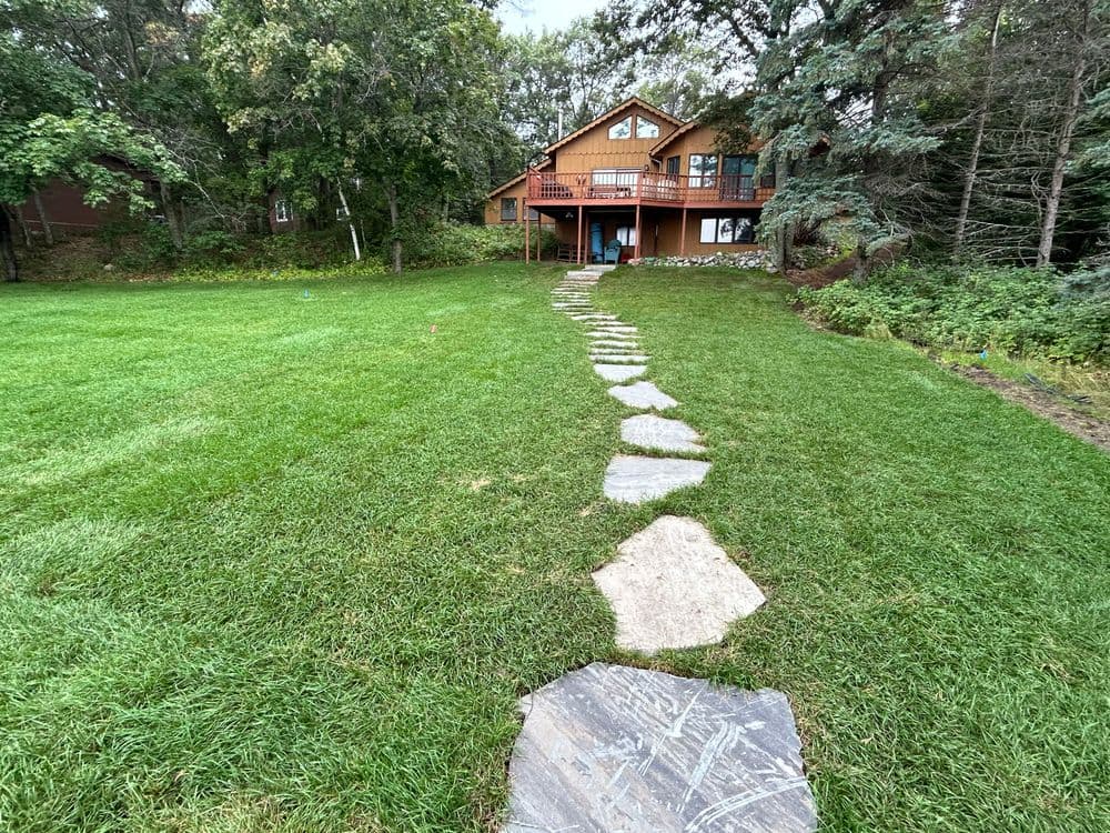 Pathway leading to a wooden house surrounded by lush green grass and trees.