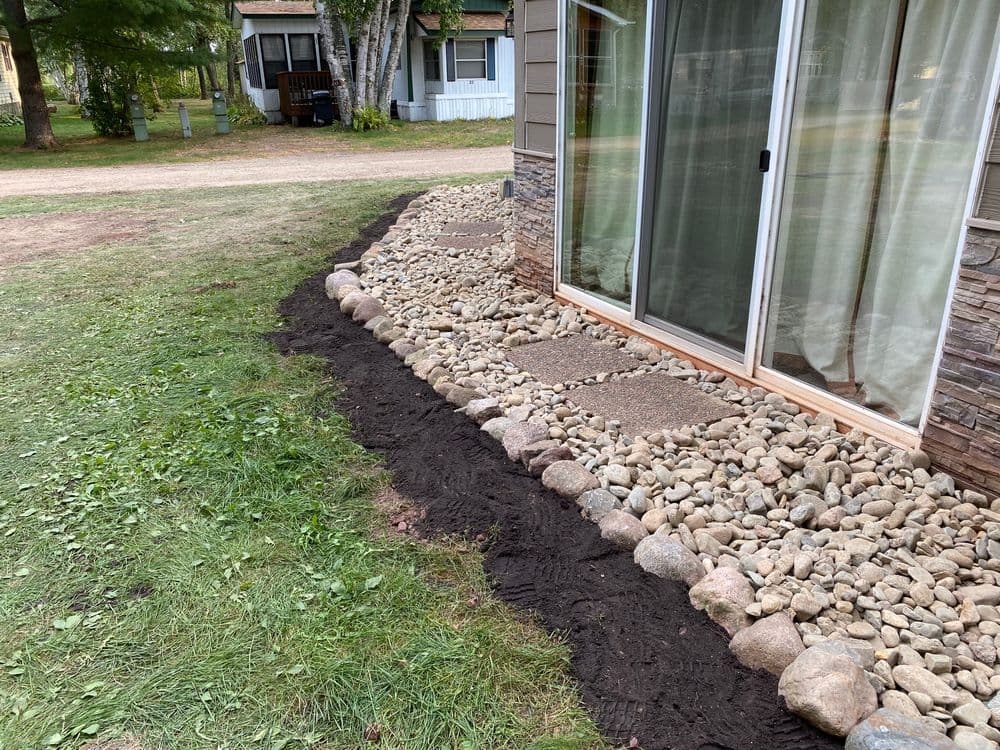 Landscaped yard with gravel and stone pathways beside a house and green lawn.