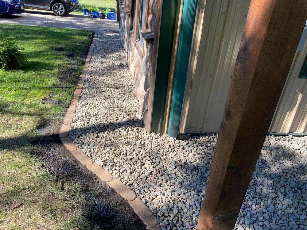 Gravel landscaping around a building with a stone and metal exterior for drainage and aesthetics.