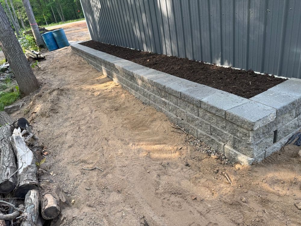Retaining wall made of gray concrete blocks with freshly laid soil for gardening.