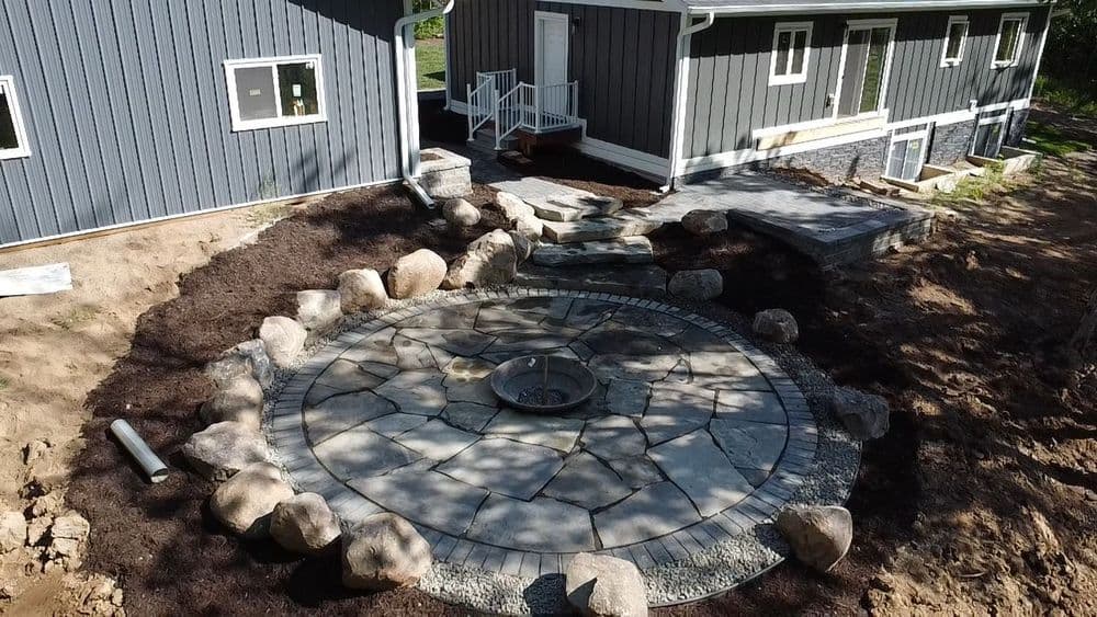 Patio with stone circle and fire pit surrounded by landscaping rocks and a modern home backdrop.