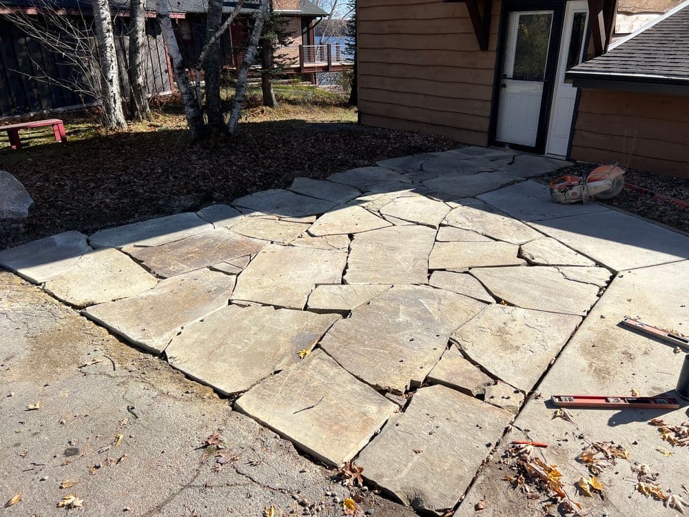 Patio with large stone slabs, showcasing broken sections and autumn leaves around.